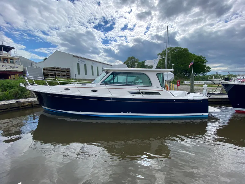 Slide: The Image of 2025 Back Cove 37 Hardtop Express yacht docked on a calm waterway under cloudy skies. - 16