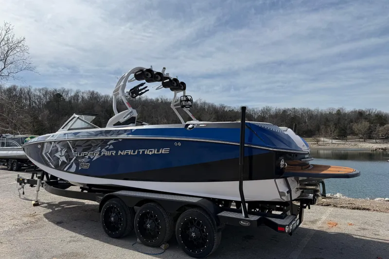 Slide: The Image of 2015 Nautique Super Air Nautique G25 boat on trailer by a lake. - 2