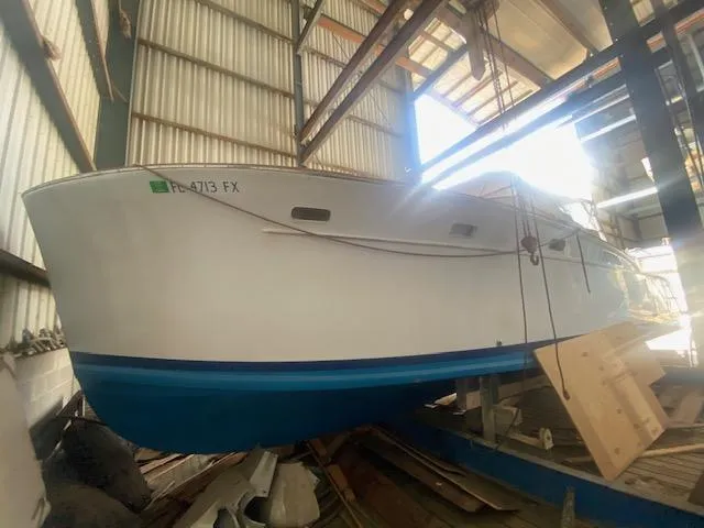 Slide: The Image of 1953 Rybovich Express boat in a warehouse, white hull with blue bottom. - 25