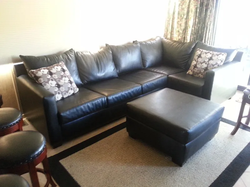 Slide: The Image of Black leather sectional sofa with floral pillows and matching ottoman in a cozy living room. - 5