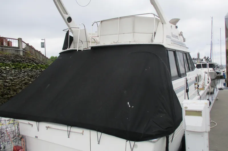 Slide: The Image of 1988 Bayliner 3888 Motoryacht docked with black cover, overcast sky. - 3