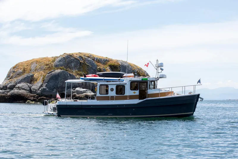 The Image of 2024 Ranger Tugs R-31 Sedan Luxury Edition boat on water near rocky island. - 0