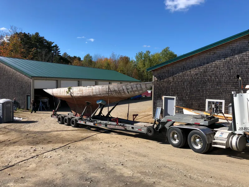 Slide: The Image of A 1903 Herreshoff Bar Harbor 31 sailboat on a trailer near a rustic building. - 6