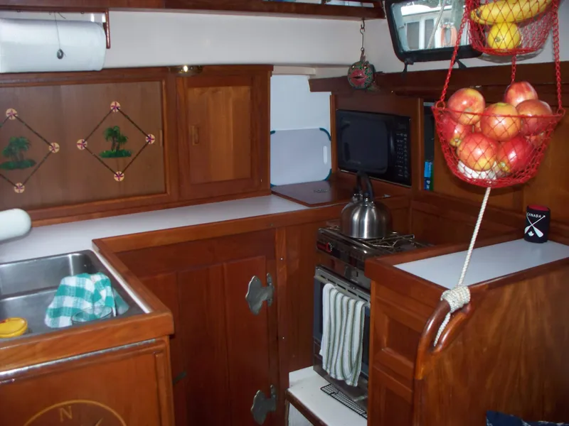 Slide: The Image of 1983 Whitby 42 sailboat galley with wooden cabinets, stove, and hanging fruit basket. - 22