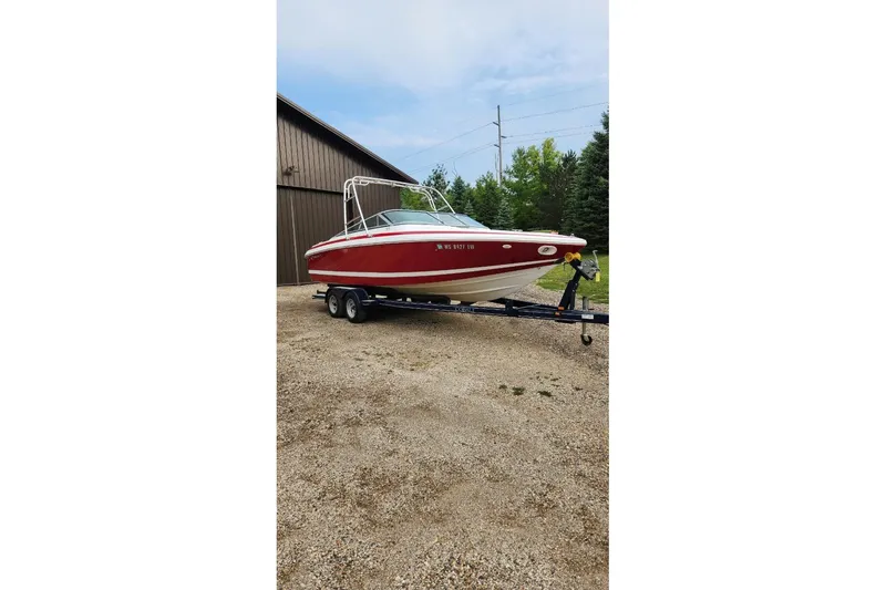 Slide: The Image of Red 2000 Cobalt 246 boat on trailer, parked near a wooden building and trees. - 2