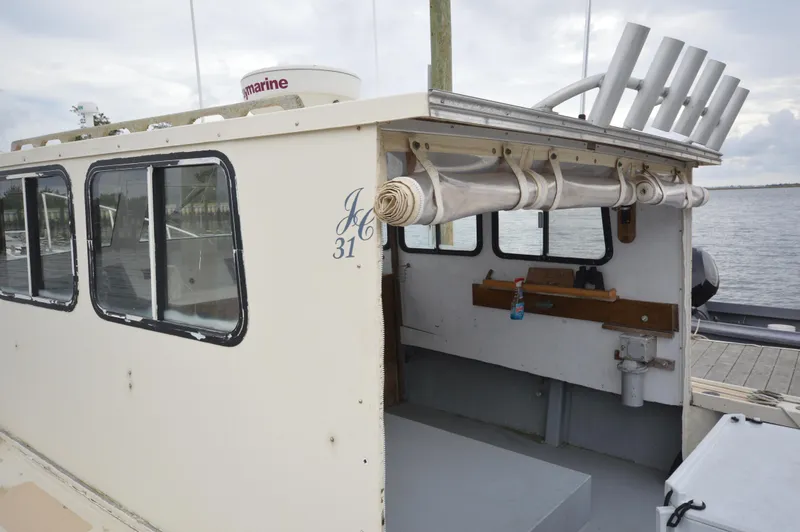 Slide: The Image of 1978 JC 31 boat with enclosed cabin and fishing rod holders, docked by the water. - 23