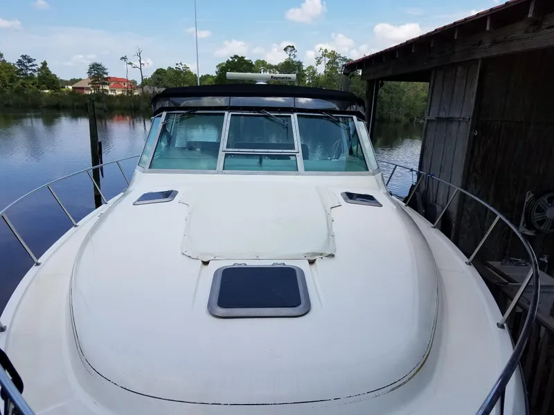 Slide: The Image of 1995 Tiara Yachts 3500 Express docked by a wooden boathouse on a calm river. - 1