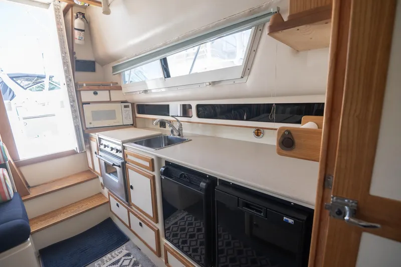 Slide: The Image of Interior of 1996 Albin 32 Command Bridge, featuring a compact kitchen with appliances and storage. - 7