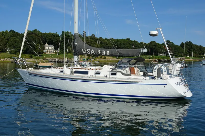 Slide: The Image of 1989 Nordic 40 sailboat on calm water, with lush green shoreline in the background. - 2