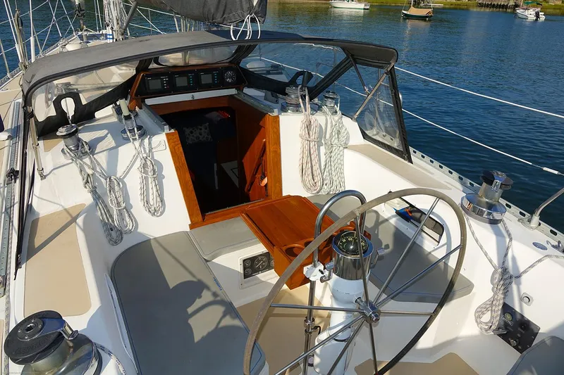 Slide: The Image of Cockpit of 1989 Nordic 40 sailboat with steering wheel and ropes, docked on calm water. - 93