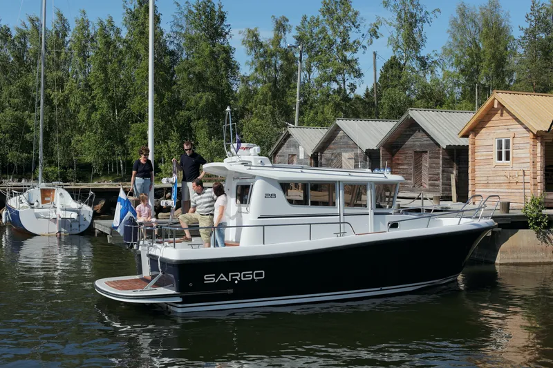 Slide: The Image of 2024 Sargo 28 boat docked with people onboard near wooden cabins. - 41