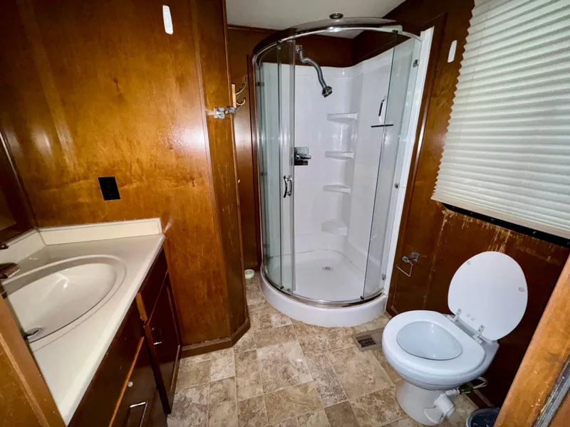 Slide: The Image of Compact RV bathroom with wood paneling, corner shower, sink, and toilet in Bravada Bella Luna Trip #16. - 21