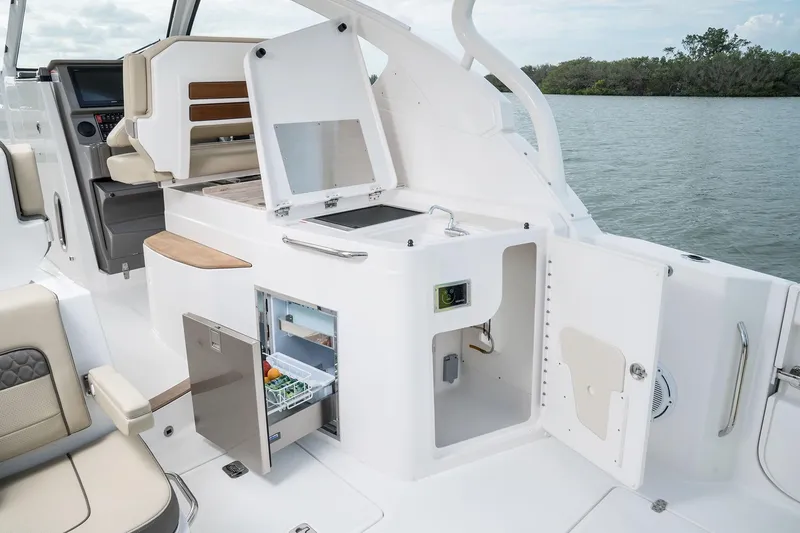 Slide: The Image of 2025 Pursuit DC 365 Dual Console boat interior with open fridge and storage compartments. - 19