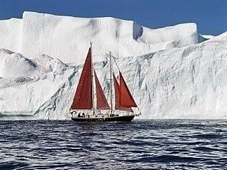 Slide: The Image of A 1979 Worldcruiser schooner sails near a massive iceberg under a clear blue sky. - 1