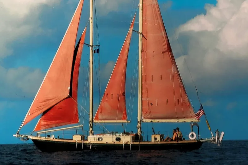 Slide: The Image of Vintage 1979 Worldcruiser schooner with red sails on open sea under blue sky. - 27