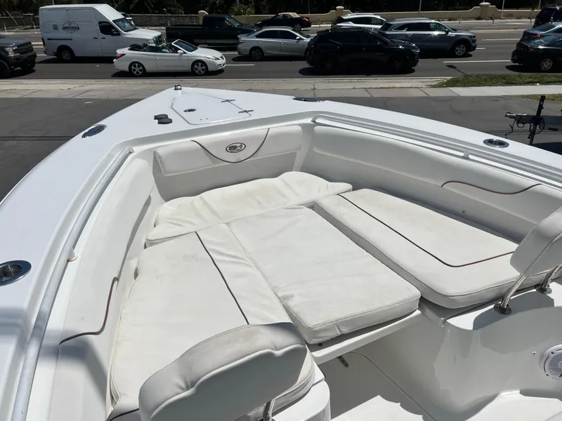 Slide: The Image of 2018 Sea Hunt Gamefish 25 boat with spacious white seating area, parked near a busy road. - 6