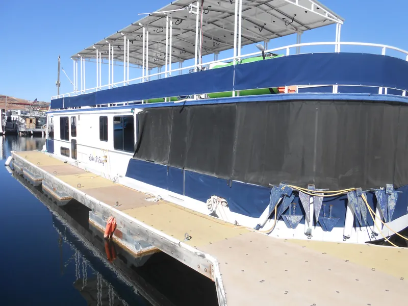Slide: The Image of 1990 Skipperliner Custom Houseboat docked, featuring a covered upper deck and blue accents. - 9