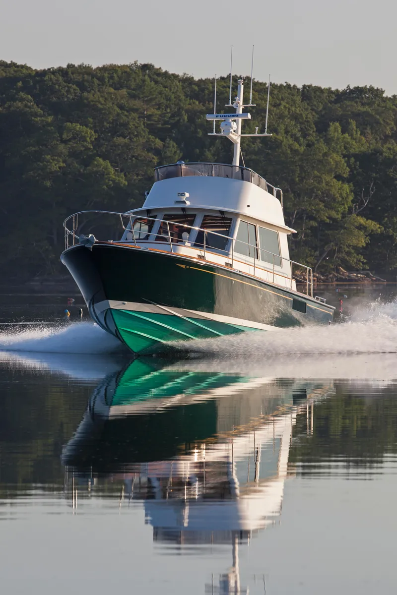 Slide: The Image of 2024 Lyman-Morse HUNT Express Cruiser Flybridge on calm water, surrounded by lush greenery. - 5