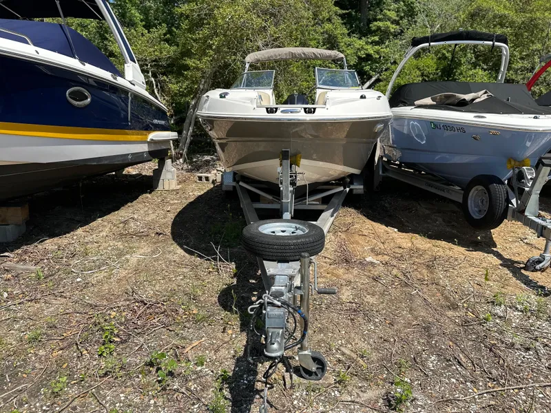Slide: The Image of 2016 Stingray 234 LR boat on trailer, parked between two other boats, surrounded by trees. - 36