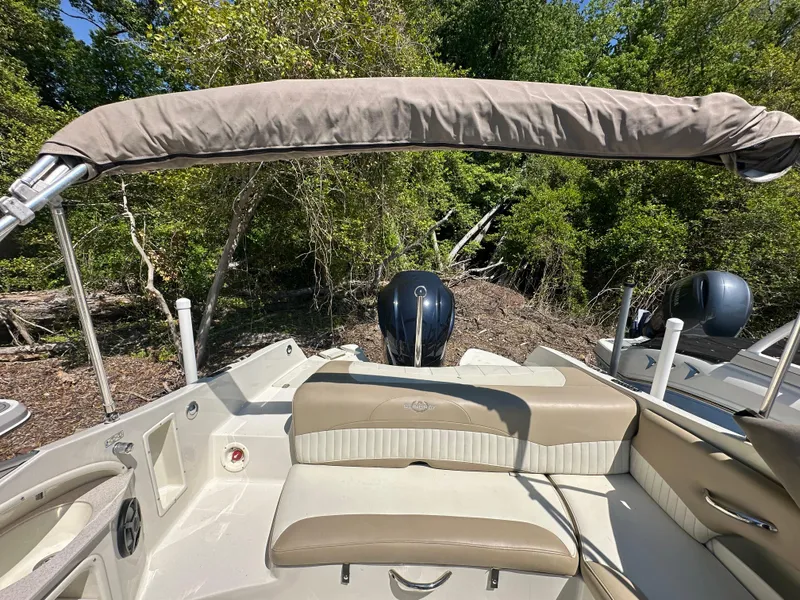 Slide: The Image of 2016 Stingray 234 LR boat interior with beige seating and canopy, surrounded by lush greenery. - 47