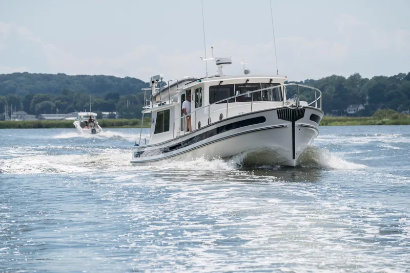 Slide: The Image of 2025 Nordic Tug 40 cruising on a scenic waterway with lush green shoreline. - 2