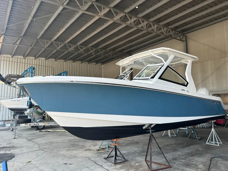 Slide: The Image of 2026 Edgewater 262CX Crossover boat in a warehouse, blue and white hull. - 3
