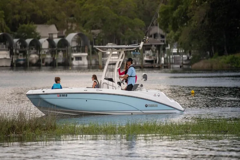 Slide: The Image of 2023 Yamaha Boats 210 FSH Sport on a serene lake with passengers. - 2