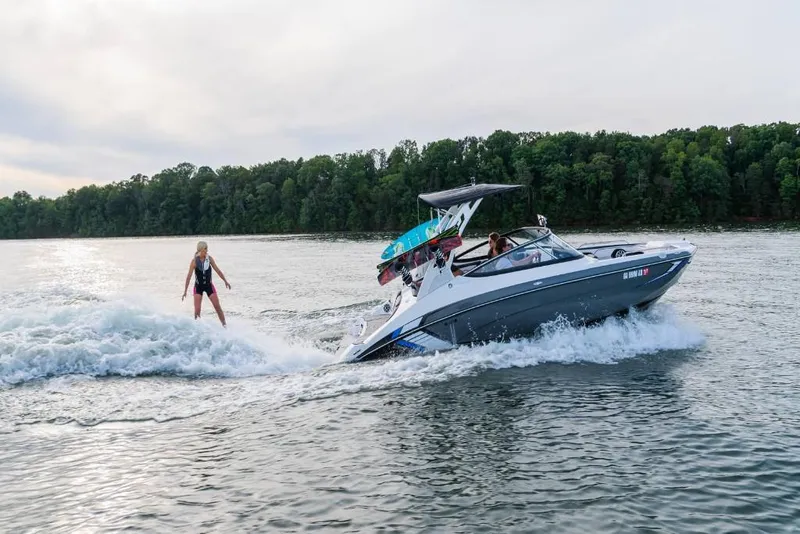 Slide: The Image of 2023 Yamaha Boats 212X towing a wakeboarder on a lake. - 2