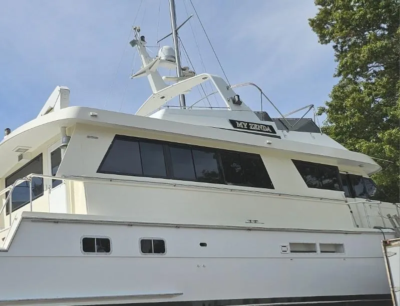 The Image of 1991 Hatteras Cockpit Motor Yacht, white exterior, docked, side view, clear sky, trees in background. - 0