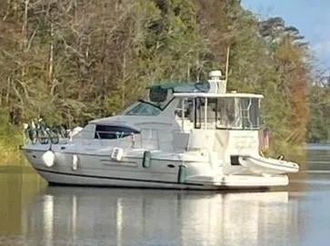 Slide: The Image of 2000 Cruisers Yachts 4450 Express Motor Yacht on calm water, surrounded by trees. - 2