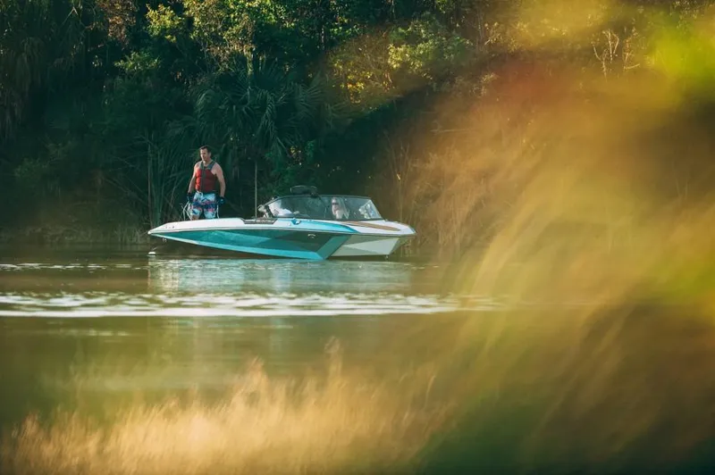 Slide: The Image of 2023 Nautique Ski boat on a serene lake with lush greenery. - 17