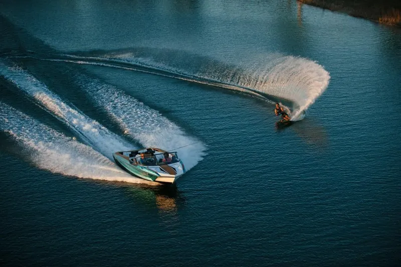 Slide: The Image of 2023 Nautique Ski boat towing a water skier on a serene lake. - 18