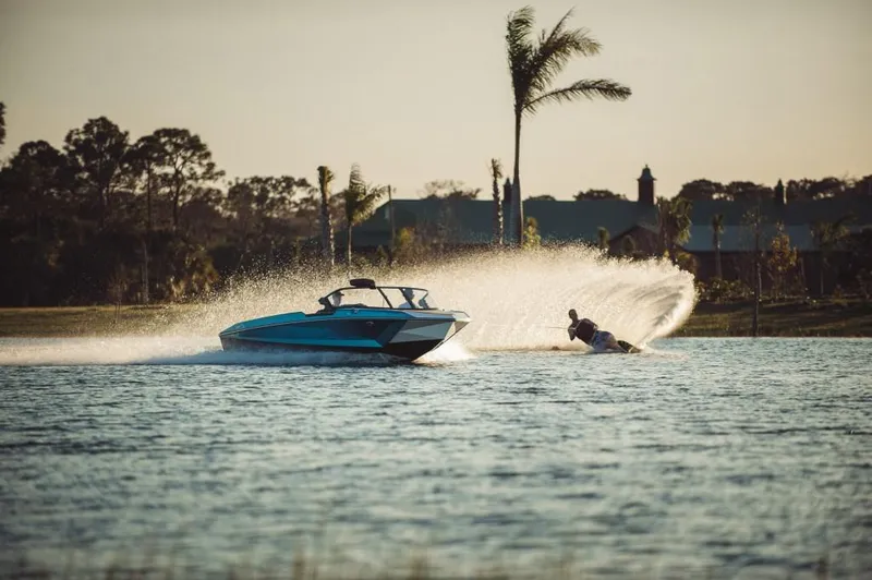 Slide: The Image of 2023 Nautique Ski boat towing a water skier on a serene lake at sunset. - 19