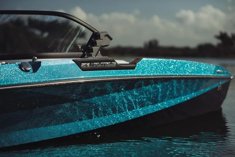Slide: The Image of 2023 Nautique Ski boat with sparkling blue exterior on calm water. - 2