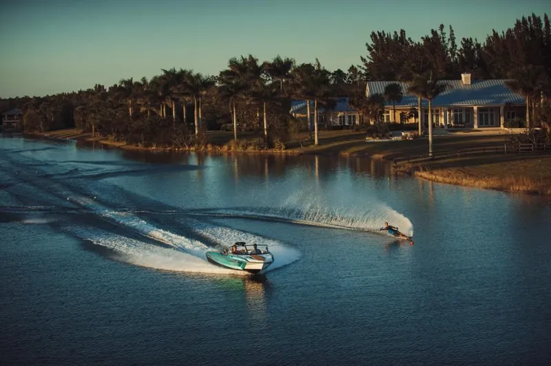 Slide: The Image of 2023 Nautique Ski boat towing a water skier on a serene lake at sunset. - 21