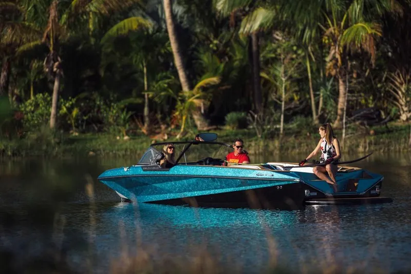 Slide: The Image of 2023 Nautique Ski boat on a serene lake with three people onboard. - 22
