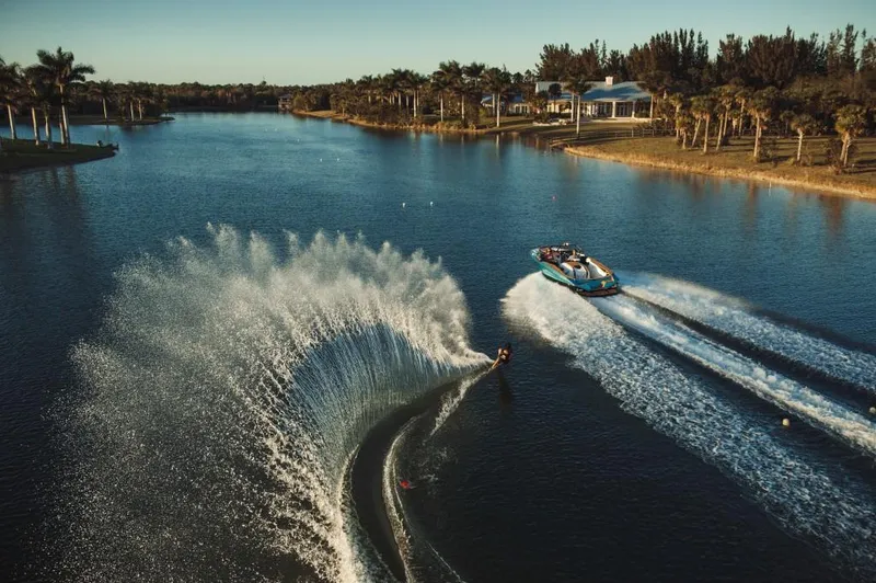 Slide: The Image of 2023 Nautique Ski boat towing a water skier on a scenic lake. - 23