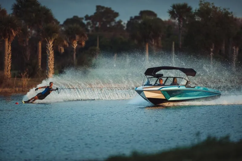 Slide: The Image of 2023 Nautique Ski boat towing a water skier on a scenic lake. - 29