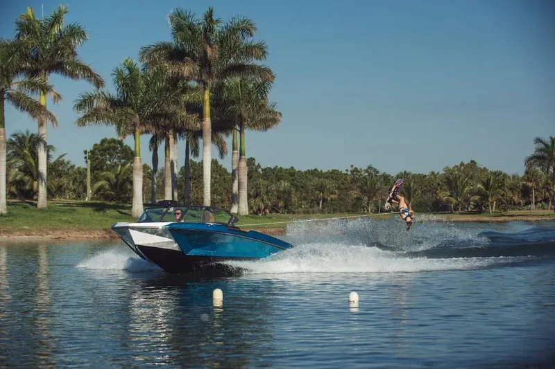 Slide: The Image of 2023 Nautique Ski boat towing a wakeboarder on a sunny lake with palm trees. - 36