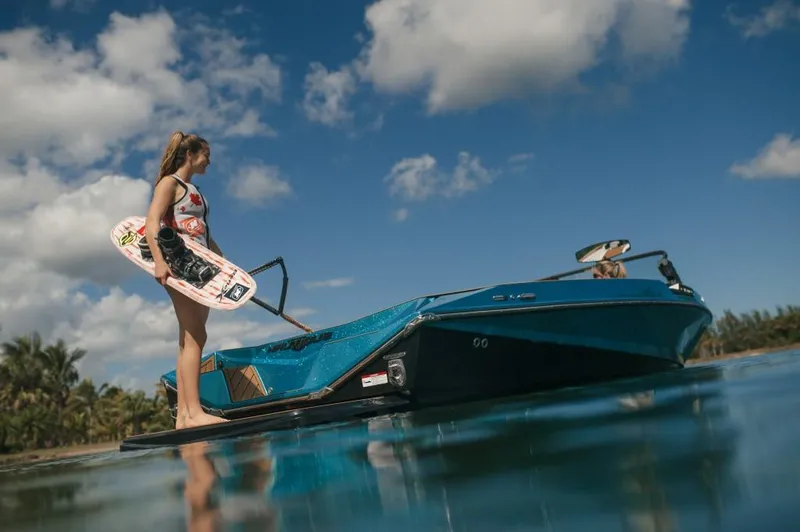 Slide: The Image of 2023 Nautique Ski boat with wakeboarder preparing to ride on a sunny day. - 4