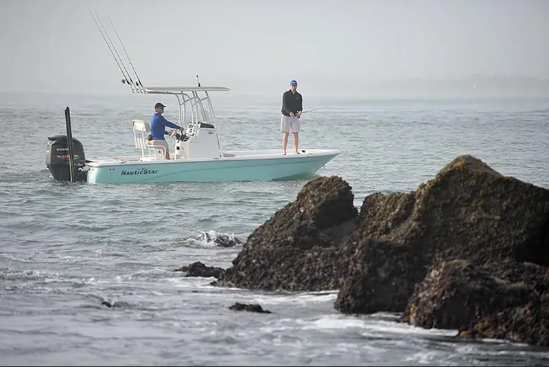 Slide: The Image of 2023 NauticStar 227 XTS boat with two people fishing near rocky shore. - 6