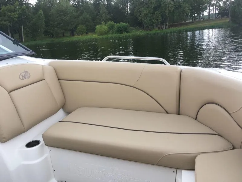 Slide: The Image of 2023 NauticStar 223DC Sport Deck boat interior with beige seating by a lake. - 10