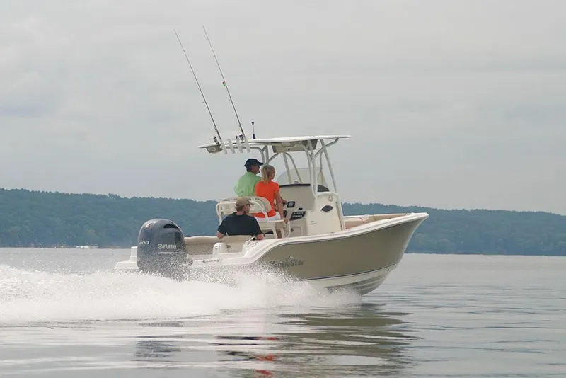 Slide: The Image of 2023 NauticStar 2302 Legacy boat cruising on a calm lake with three passengers. - 11