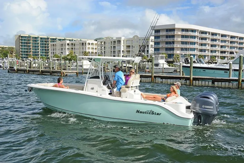 Slide: The Image of 2023 NauticStar 2602 Legacy boat cruising near a marina with modern buildings in the background. - 3