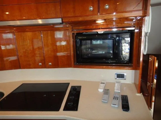 Slide: The Image of 2004 Riviera 58 Enclosed Flybridge kitchen with microwave, stove, and remote controls. - 28