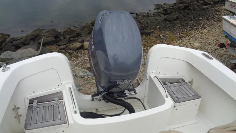 Slide: The Image of 2008 Roth Bilt 21 Classic boat with outboard motor, docked by rocky shoreline. - 10