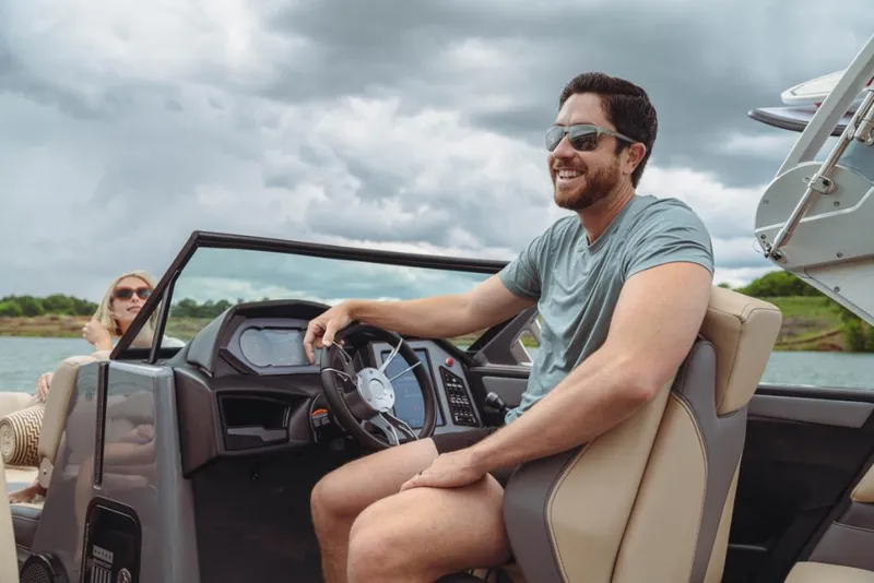 Slide: The Image of Man driving 2023 MasterCraft XStar boat on a lake, smiling under cloudy sky. - 10