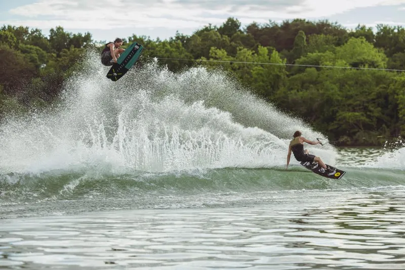 Slide: The Image of 2023 MasterCraft XStar wakeboarding on a lake with two riders performing tricks. - 15
