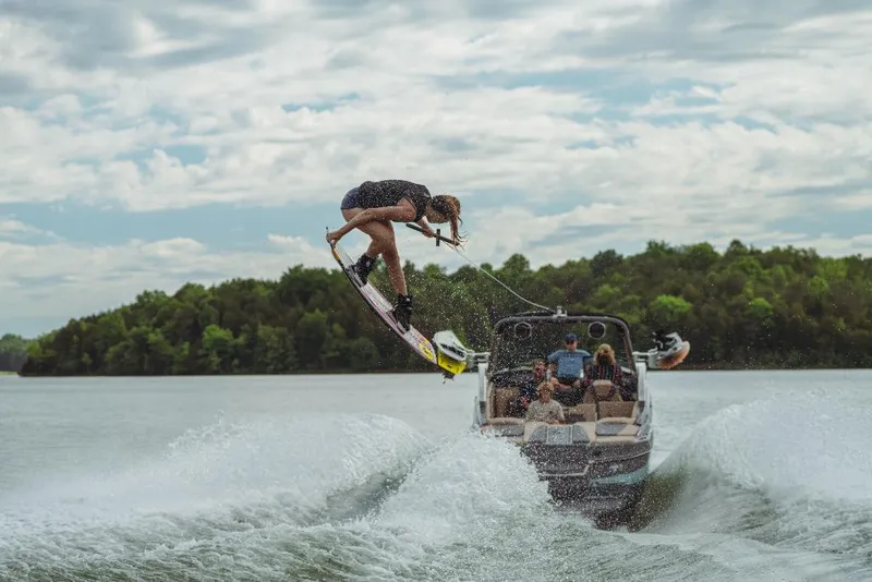 Slide: The Image of 2023 MasterCraft XStar boat towing a wakeboarder performing a jump on a lake. - 5