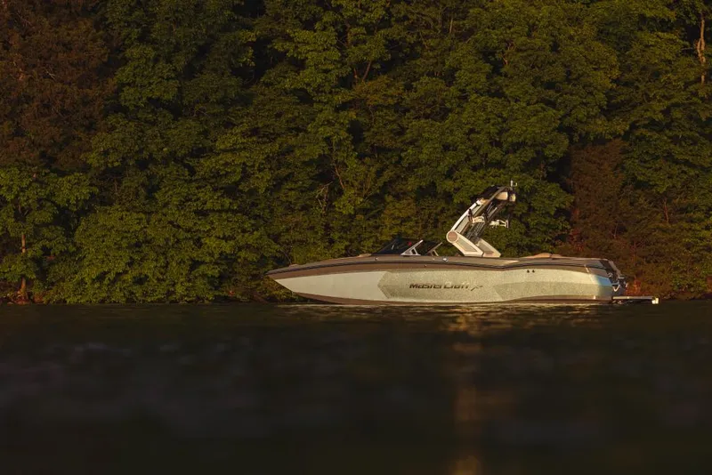 Slide: The Image of 2023 MasterCraft XStar boat on a calm lake with a forest backdrop. - 6
